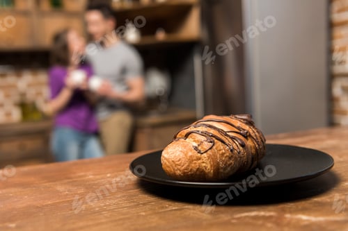 Preview: couple with coffee in kitchen, plate with croissant on foreground