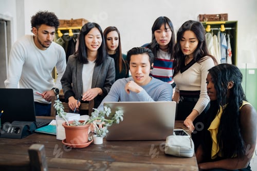 Preview: Group of young businessmen and women looking at laptop in office meeting