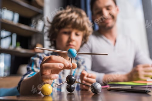 Preview: selective focus of father and preteen son playing with atoms model at home