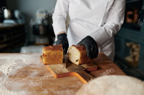 Preview: Baker chef holding knife and cutting fresh bread on wooden table