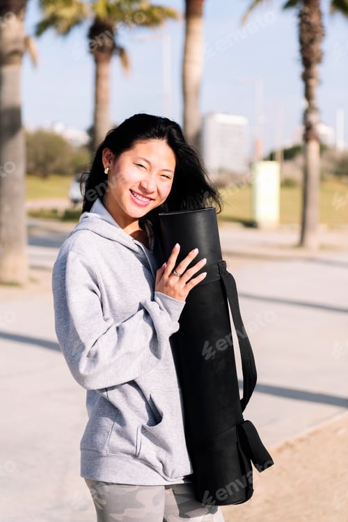 Preview: young asian woman smiling while holding yoga mat