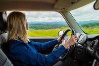 Preview: Blonde woman is driving a car with mountains on background