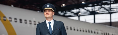 Preview: Thoughtful pilot in uniform looking away, standing in front of big passenger airplane in airport