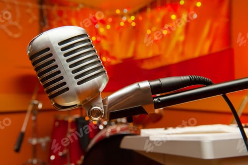 Preview: Closeup shot of a retro microphone with musical instruments in the background against a red wall