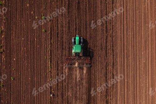 Preview: Green tractor vehicle with tiller attached performing field tillage before the sowing season