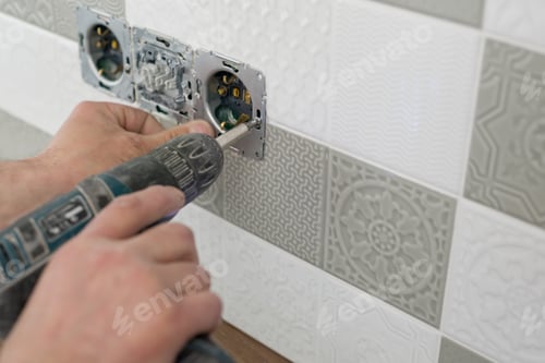 Preview: Close-up of electricians hand installing outlet on wall with ceramic tiles