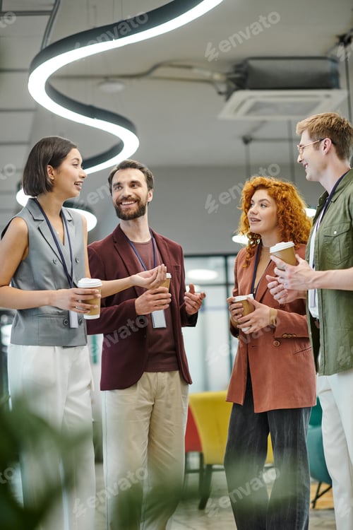 Preview: young businesswoman talking to cheerful colleagues with paper cups, coffee break in modern office