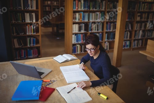 Preview: Female student studying with laptop, notebooks and textbooks on wooden table in library, copy space