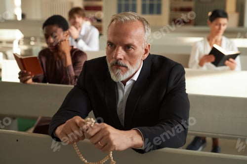 Preview: Senior Man Praying and Holding Rosary in Church on Sunday