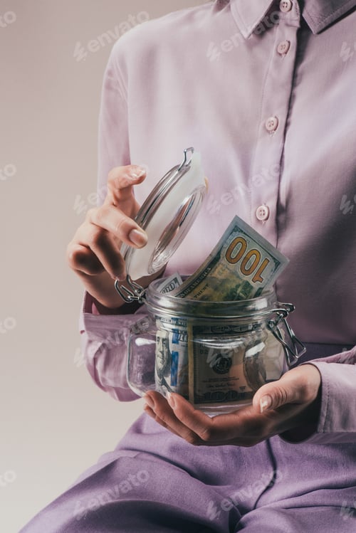 Preview: partial view of woman holding glass jar with savings isolated on lilac