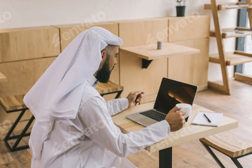 Preview: concentrated muslim man in cafe looking at laptop