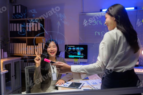Preview: Two businesswomen working late at night using a glass board to discuss and brainstorm ideas
