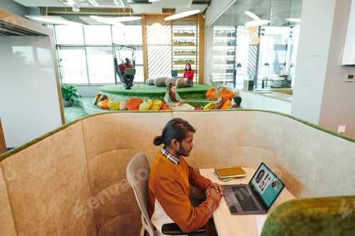 Preview: Young serious mixed-race businessman networking by desk in office environment