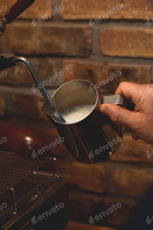 Preview: Restaurant employee, male barista is making espresso and frothing milk