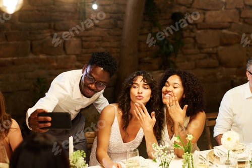 Preview: Happy young African American man with smartphone making selfie with brides