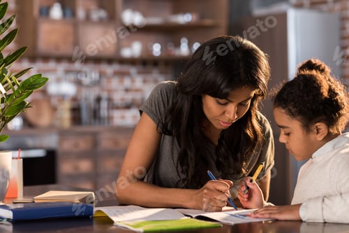 Preview: Mother and cute little daughter sitting at table and doing homework together at home, homework help