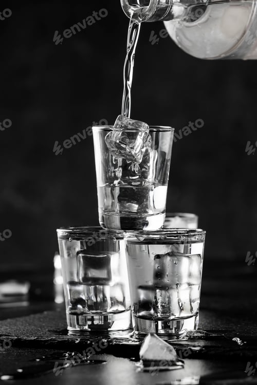 Preview: Vodka in shot glasses pouring out of the bottle on black stone background, iced strong drink