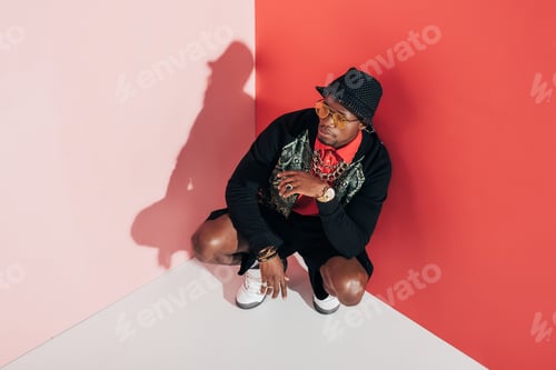 Vista previa: high angle view of stylish african american man crouching and looking away in studio