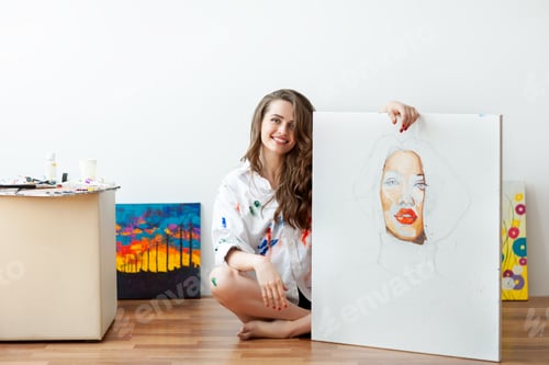 Visualização: Young smiling woman artist sits on floor with unfinished masterpiece