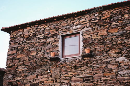 Preview: Closeup shot of a stone building with a window and two flower pots in Portugal