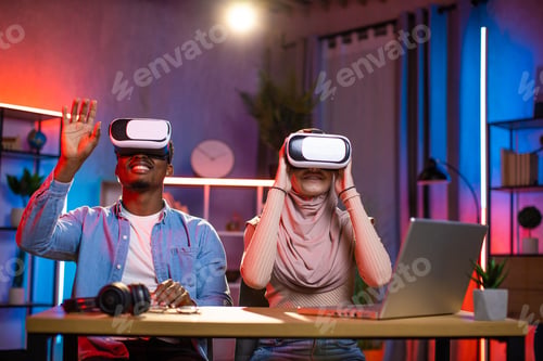 Preview: Diverse couple sitting at desk in VR glasses playing games