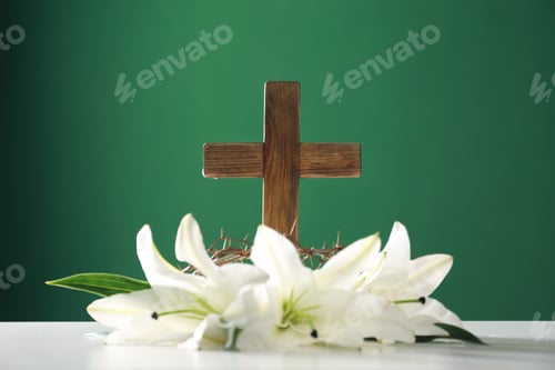 Preview: Wooden cross, crown of thorns and blossom lilies on table against color background