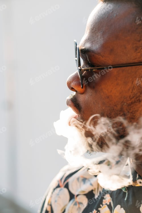 Preview: Black stylish man wearing sunglasses. He is vaping with an electronic cigarrete outdoor