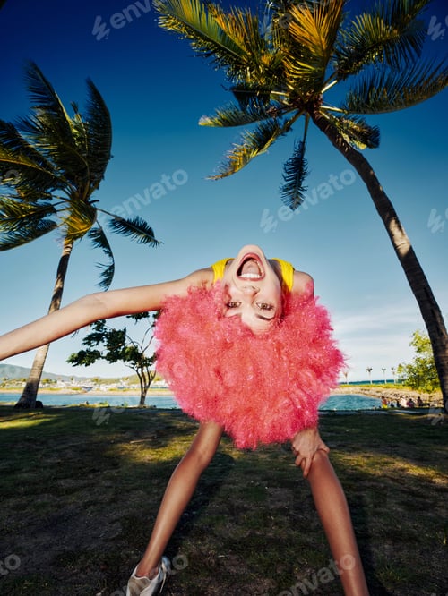 Preview: A woman with vibrant pink hair performs a handstand in front of a tall palm tree, situated in a lush
