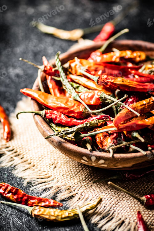 Preview: Pods of dried chili peppers in a wooden plate on a napkin.