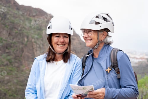 Preview: Senior women hikers with protective helmets standing on the top of mountain in a trekking day