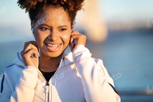 Preview: Smiling Young Black Woman Wearing Earphones Listening Music Outdoors