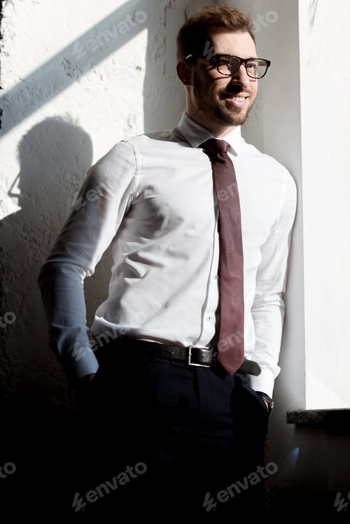 Preview: happy businessman in tie and glasses posing near white wall