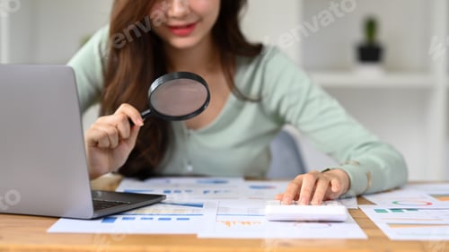 Preview: Cropped imaged of female auditor inspecting financial document with a magnifying glass.