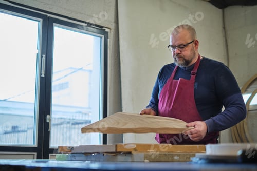Preview: The woodworker holds up a piece, eyeing the grain and form. This moment captures the essence of
