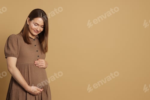 Preview: Happy young pregnant woman on light brown background. Space for text