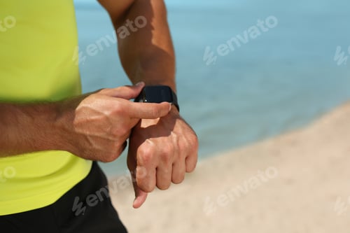 Preview: Young man checking pulse with smartwatch after training on beach, closeup. Space for text