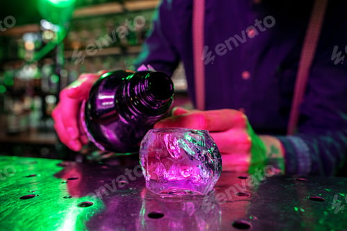Preview: Close up of barman finishes preparation of alcoholic cocktail, pouring drink in multicolored neon