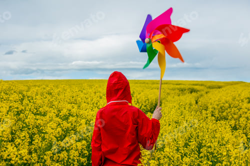 Preview: Woman in red tracksuit with colored pinwheel in rapeseed field