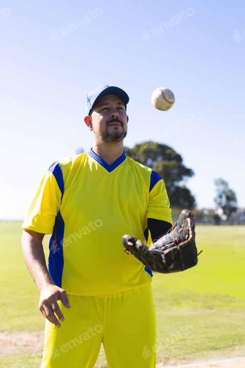 Preview: Man standing on grassy field tracking baseball over leather glove in yellow uniform and cap