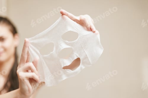 Preview: Young woman holding a facial sheet mask with a cheerful expression, preparing for a self-care