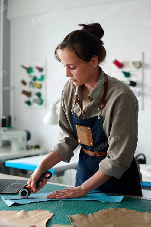 Preview: Young female artisan in workwear bending over table during work