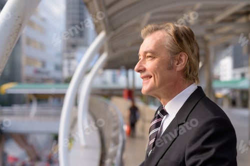 Preview: Profile view of happy mature handsome businessman looking at view of the city