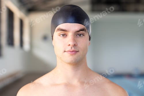 Preview: Caucasian young male swimmer standing by pool indoors, wearing black cap
