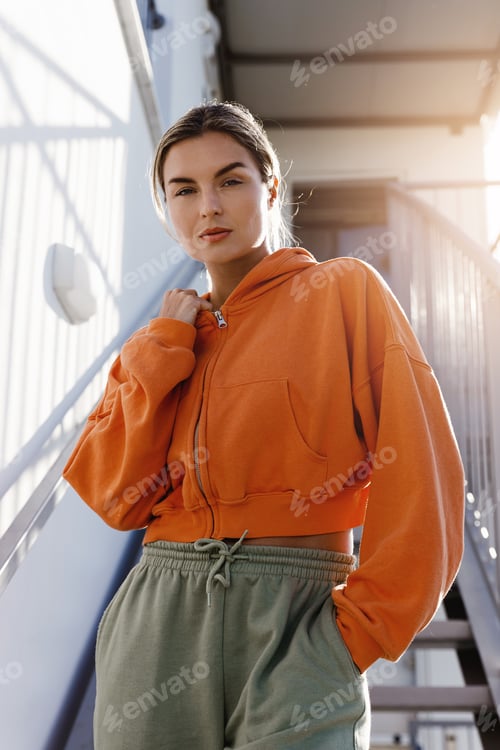 Preview: Young Woman Fitness Enthusiast Wearing an Orange Hoodie Resting Outdoors