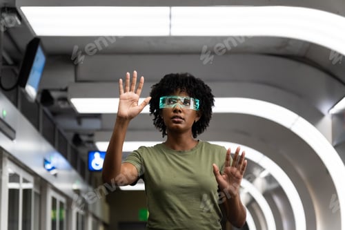 Preview: Serious afro woman wearing virtual reality simulators gesturing in futuristic metro station