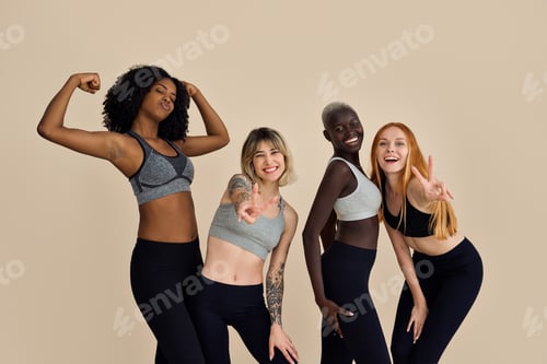 Preview: Happy fit diverse young women group having fun at beige background.