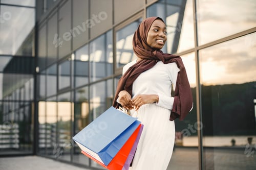 Preview: Arabic woman wearing hijab standing with shopping bags near mall