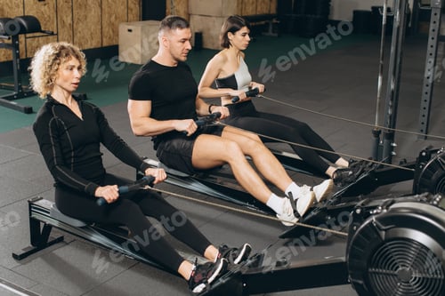 Preview: Young man and beautiful women working out with rowing machine at crossfit gym.