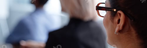 Preview: Header Image of Woman with Glasses Attending Conference Indoors