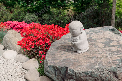 Preview: Small stone monk statue on rock in Japanese garden with red flowers